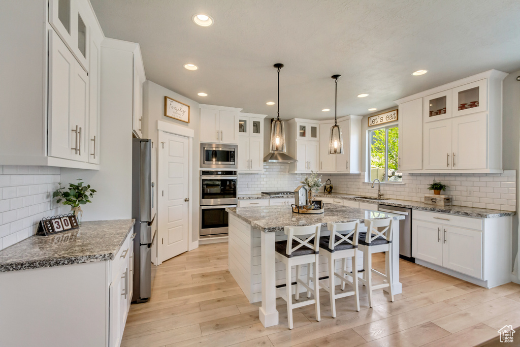 Kitchen featuring wall chimney range hood, a sink, stainless steel appliances, white cabinetry, and tasteful backsplash