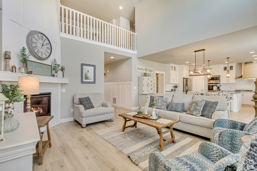 Living room with recessed lighting, a high ceiling, a large fireplace, and light wood finished floors