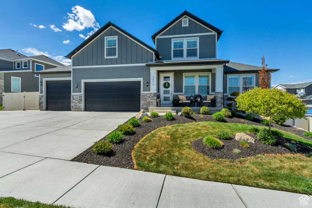 Craftsman house featuring a garage, covered porch, stone siding, board and batten siding, and driveway