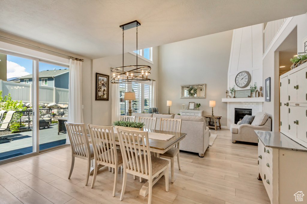 Dining room featuring an inviting chandelier, a high ceiling, a brick fireplace, and light wood-type flooring