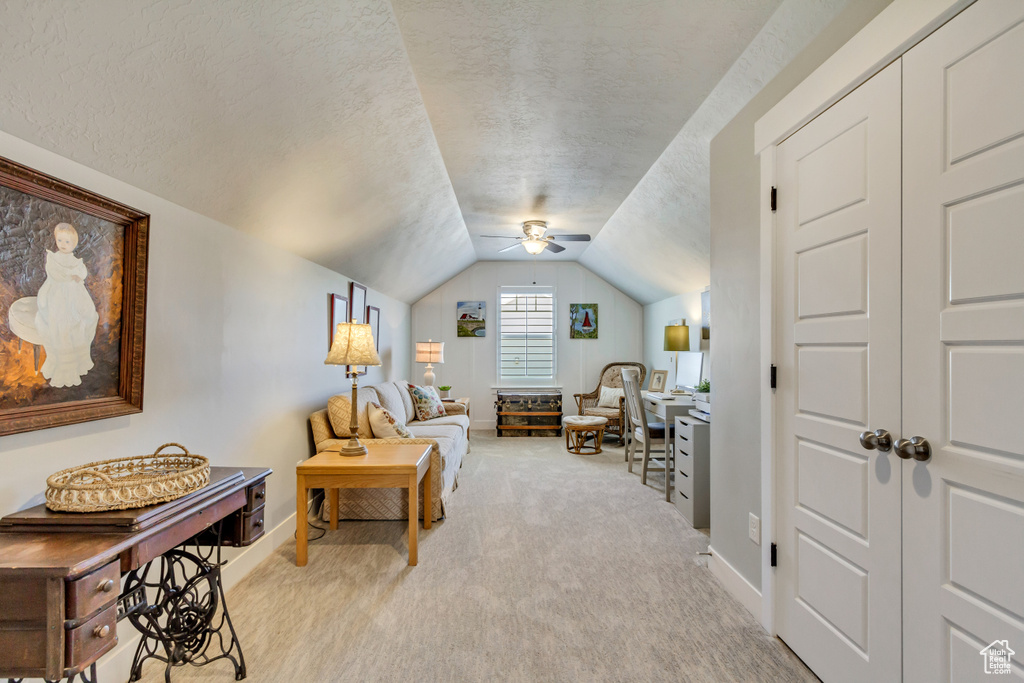 Living area featuring lofted ceiling, light carpet, baseboards, ceiling fan, and a textured ceiling
