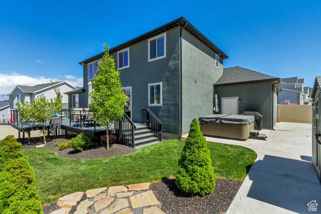Back of property with a wooden deck, stucco siding, a patio area, a lawn, and a hot tub
