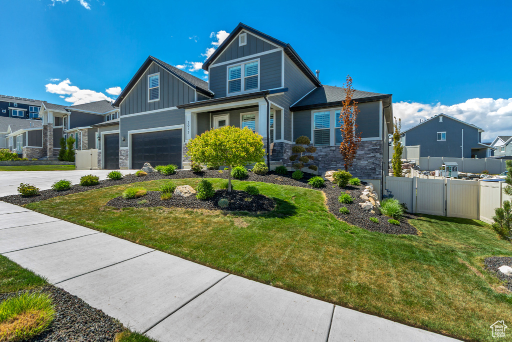Craftsman-style house featuring board and batten siding, driveway, a gate, fence, and stone siding
