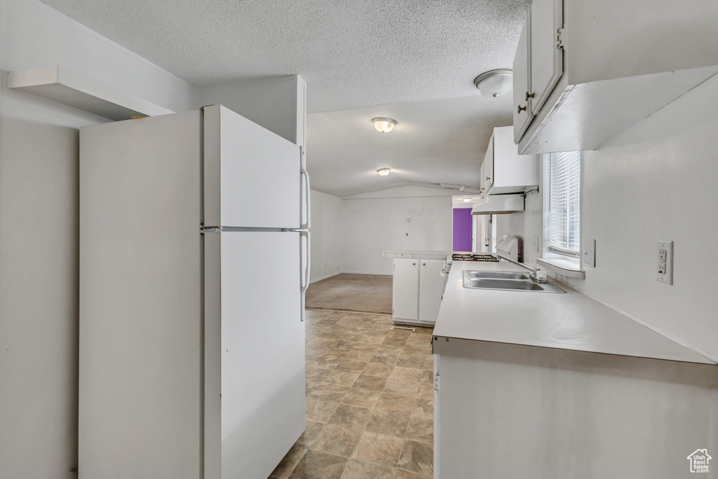 Kitchen featuring stone finish floor, vaulted ceiling, a sink, white cabinets, and freestanding refrigerator