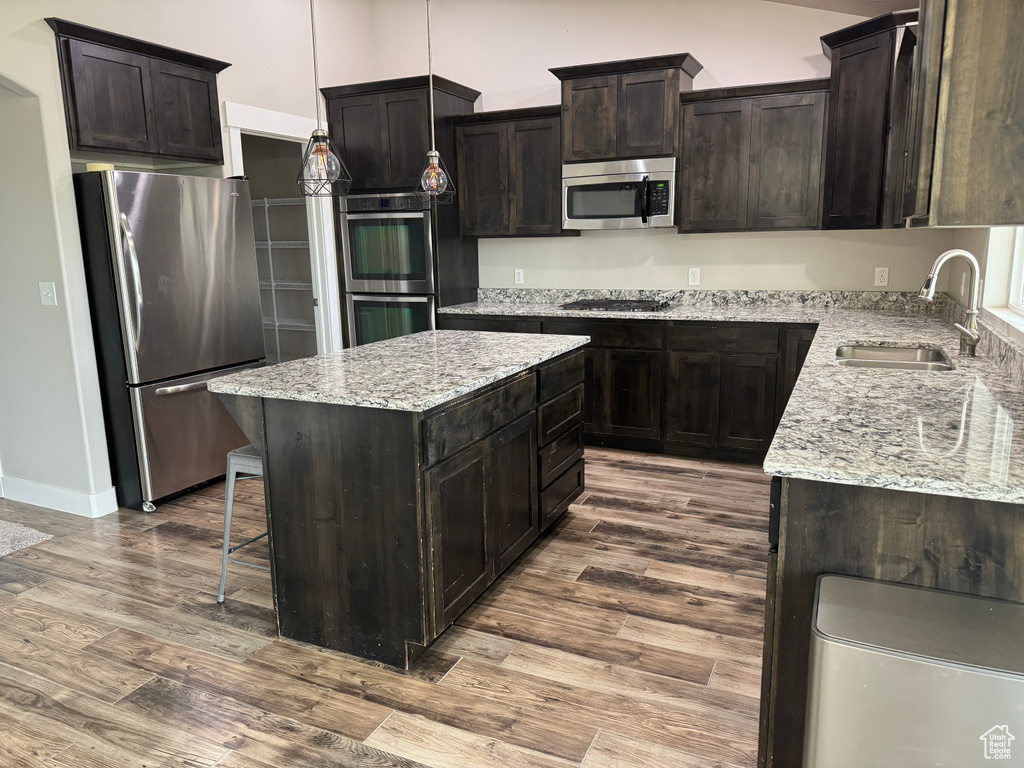 Kitchen with stainless steel appliances, a sink, dark wood-style flooring, a center island, and light stone counters