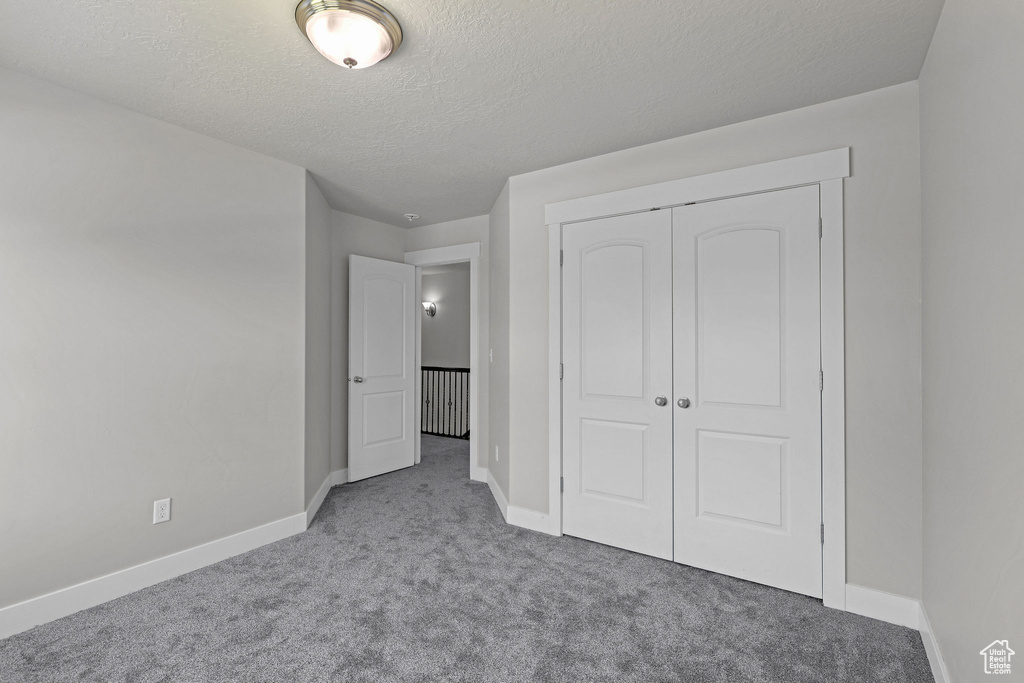 Unfurnished bedroom featuring carpet floors, a textured ceiling, baseboards, and a closet