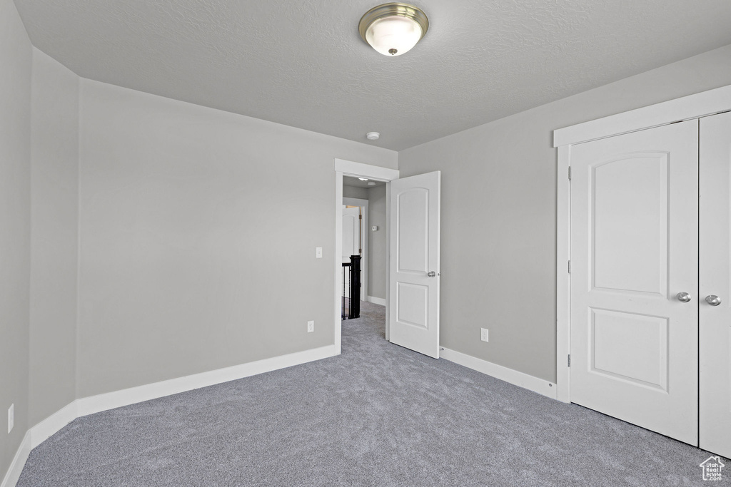 Unfurnished bedroom with carpet floors, a textured ceiling, baseboards, and a closet