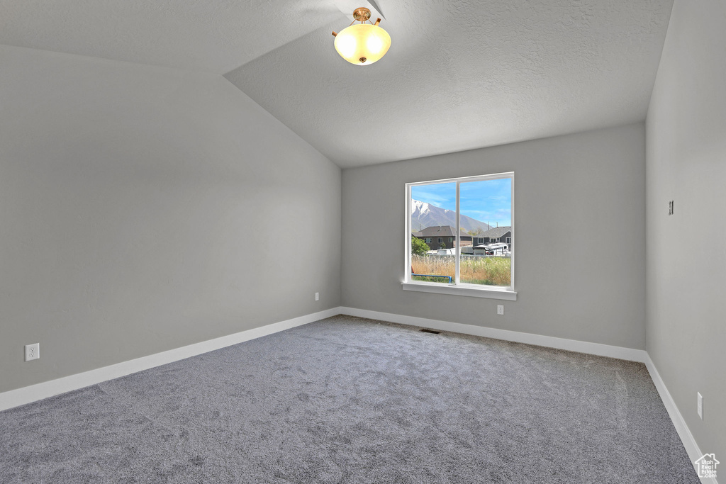 Carpeted spare room featuring baseboards, a textured ceiling, lofted ceiling, and visible vents