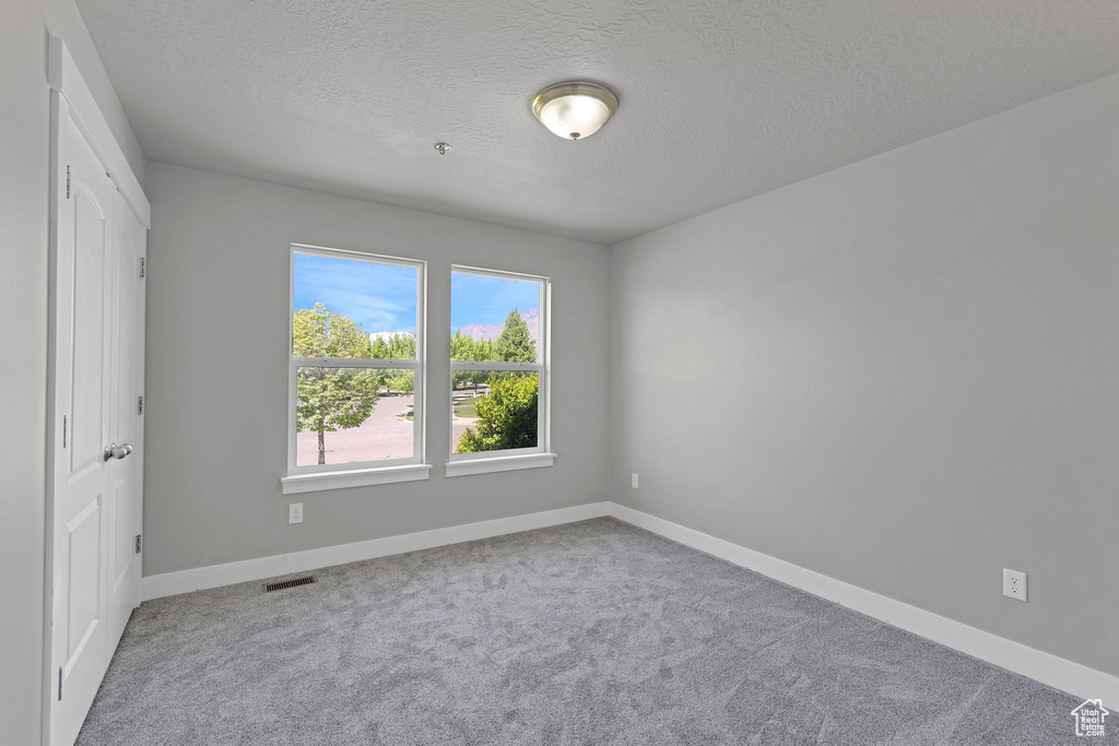Unfurnished bedroom featuring a textured ceiling, visible vents, baseboards, and carpet