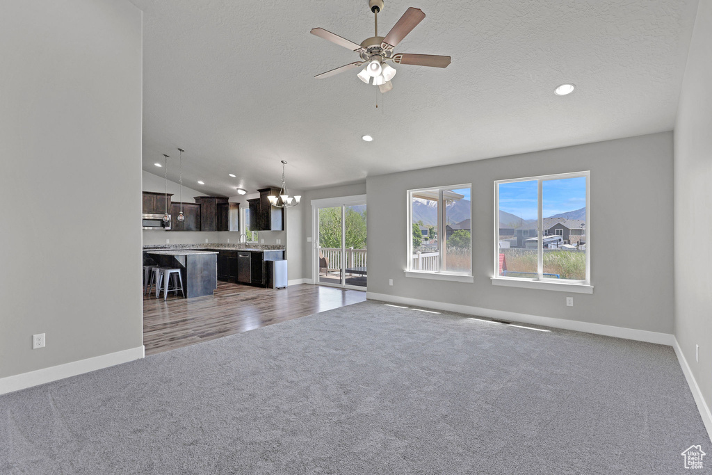 Unfurnished living room featuring carpet, ceiling fan with notable chandelier, recessed lighting, baseboards, and lofted ceiling