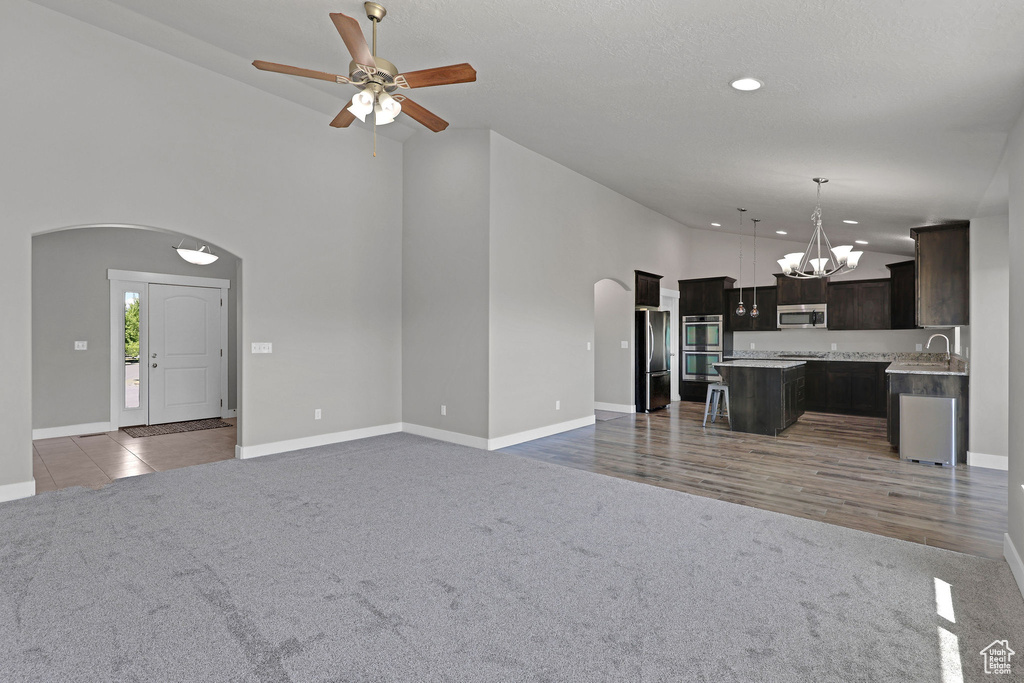 Unfurnished living room with arched walkways, a sink, high vaulted ceiling, and light carpet