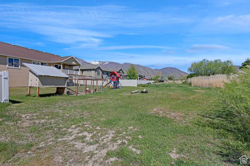 View of yard with exterior structure, fence, a playground, a mountain view, and an outbuilding