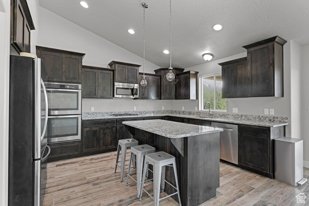 Kitchen featuring a sink, light wood finished floors, a center island, stainless steel appliances, and vaulted ceiling