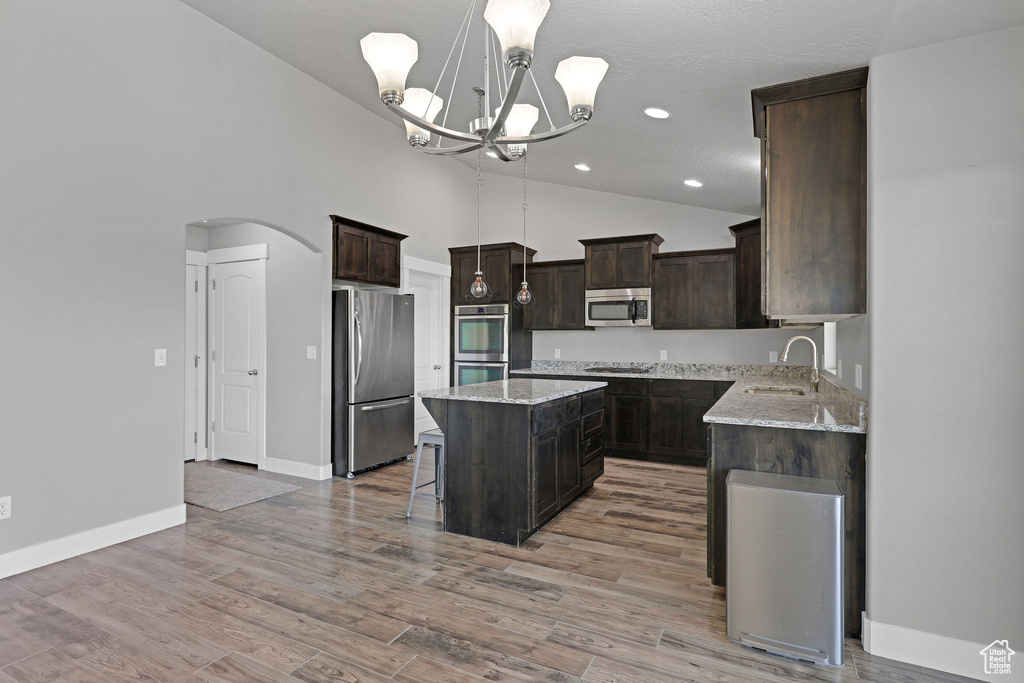 Kitchen with dark brown cabinetry, appliances with stainless steel finishes, a sink, arched walkways, and a center island