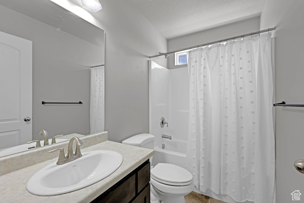 Full bath with toilet, a textured ceiling, shower / bath combo, and vanity
