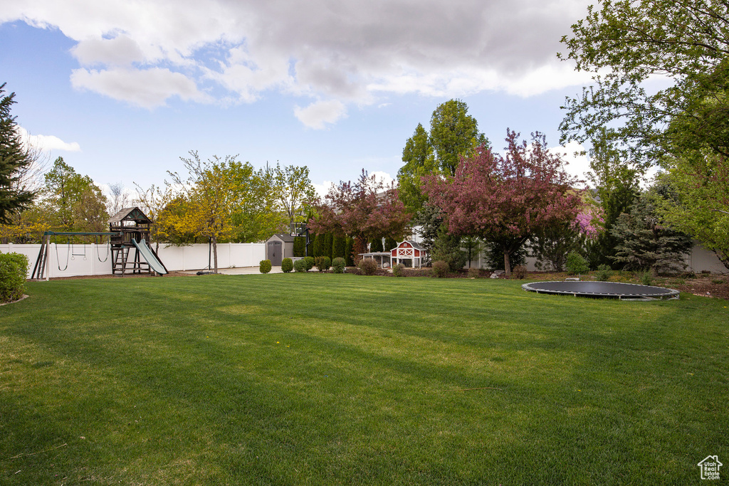 View of yard with fence, a trampoline, a shed, an outbuilding, and a playground