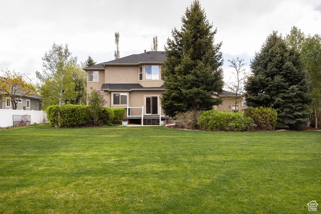 Rear view of property with fence, a wooden deck, stucco siding, and a yard