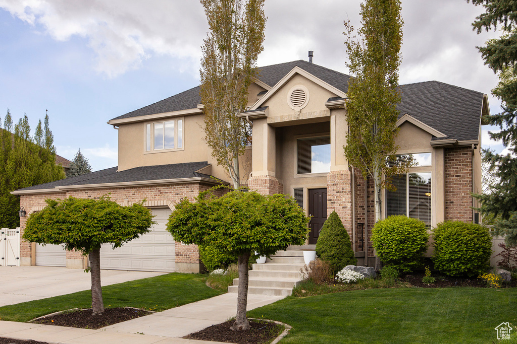 View of front of property with brick siding, a front lawn, stucco siding, and concrete driveway