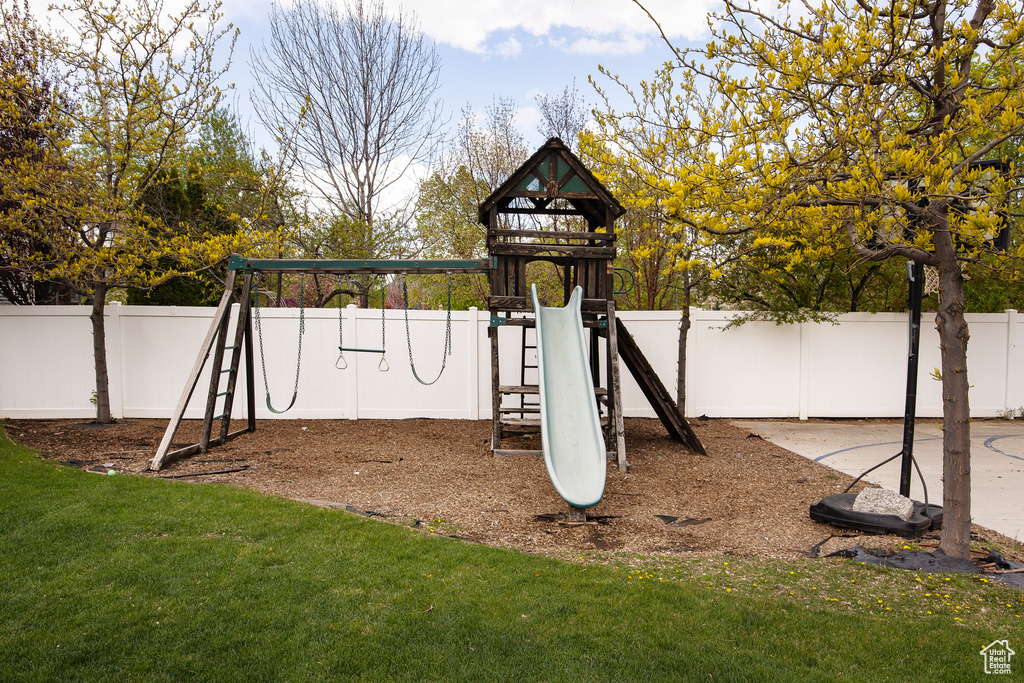 View of jungle gym featuring fence and a lawn