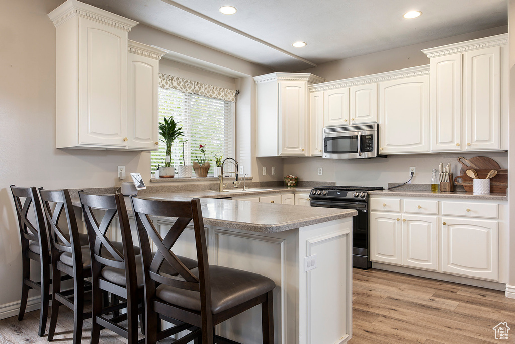 Kitchen featuring range with gas stovetop, a peninsula, a kitchen breakfast bar, stainless steel microwave, and a sink