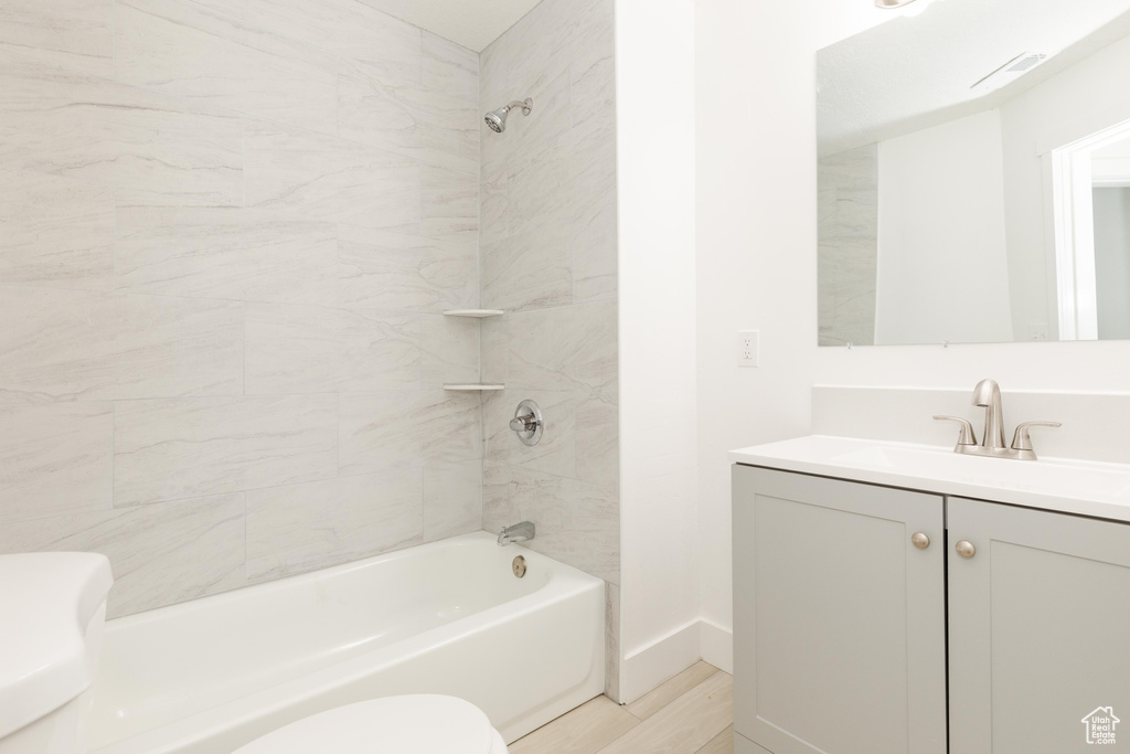Full bath with shower / bath combination, wood finished floors, vanity, baseboards, and toilet