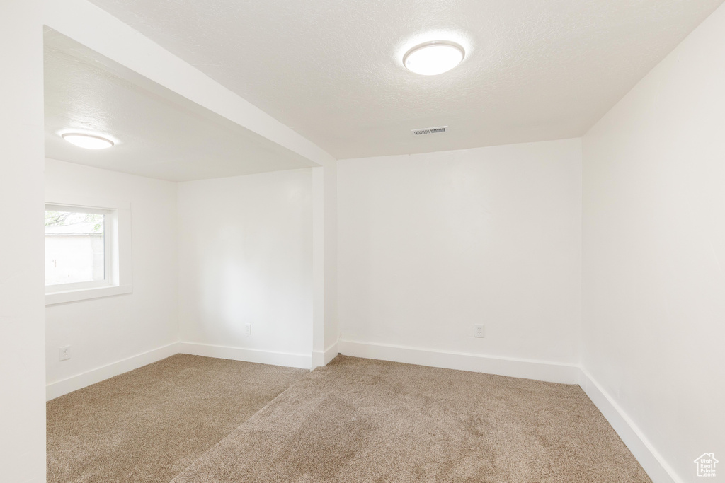 Empty room featuring a textured ceiling, visible vents, light carpet, and baseboards