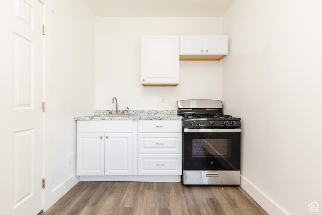 Kitchen featuring stainless steel gas range, a sink, white cabinetry, baseboards, and wood finished floors