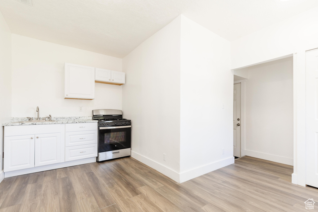 Kitchen with white cabinets, a sink, gas stove, light wood-style floors, and baseboards