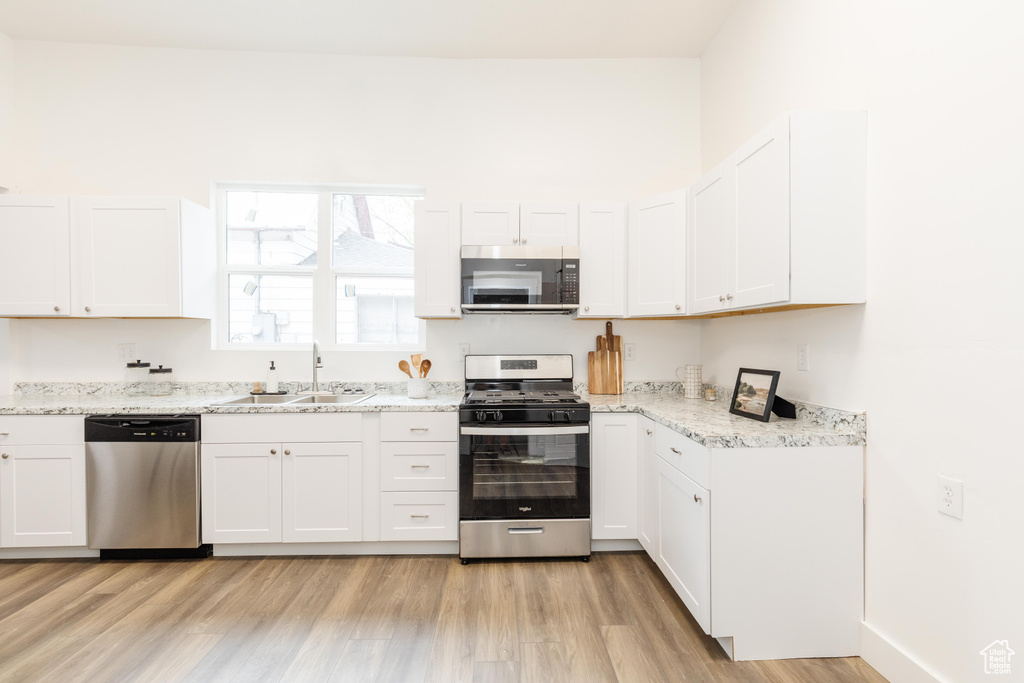 Kitchen featuring light stone countertops, stainless steel appliances, light wood-style floors, a sink, and white cabinetry