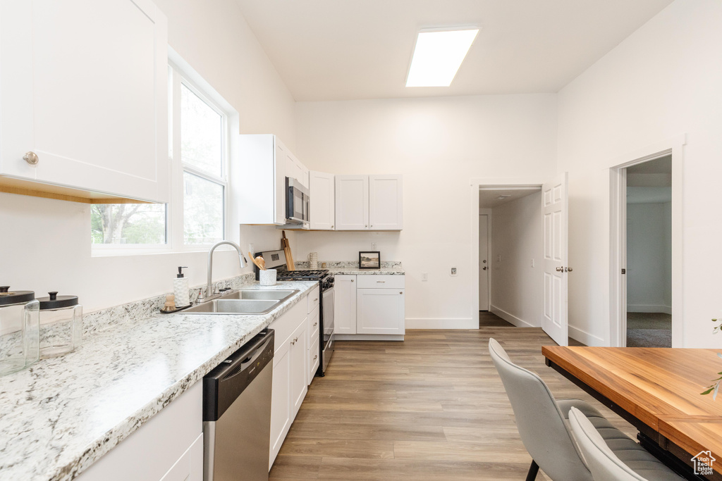 Kitchen with light stone counters, appliances with stainless steel finishes, white cabinets, a sink, and light wood-type flooring