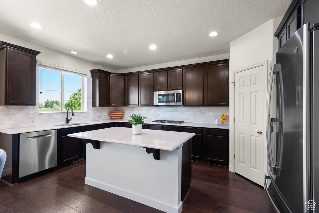 Kitchen featuring dark wood-style flooring, dark brown cabinetry, a center island, a sink, and appliances with stainless steel finishes