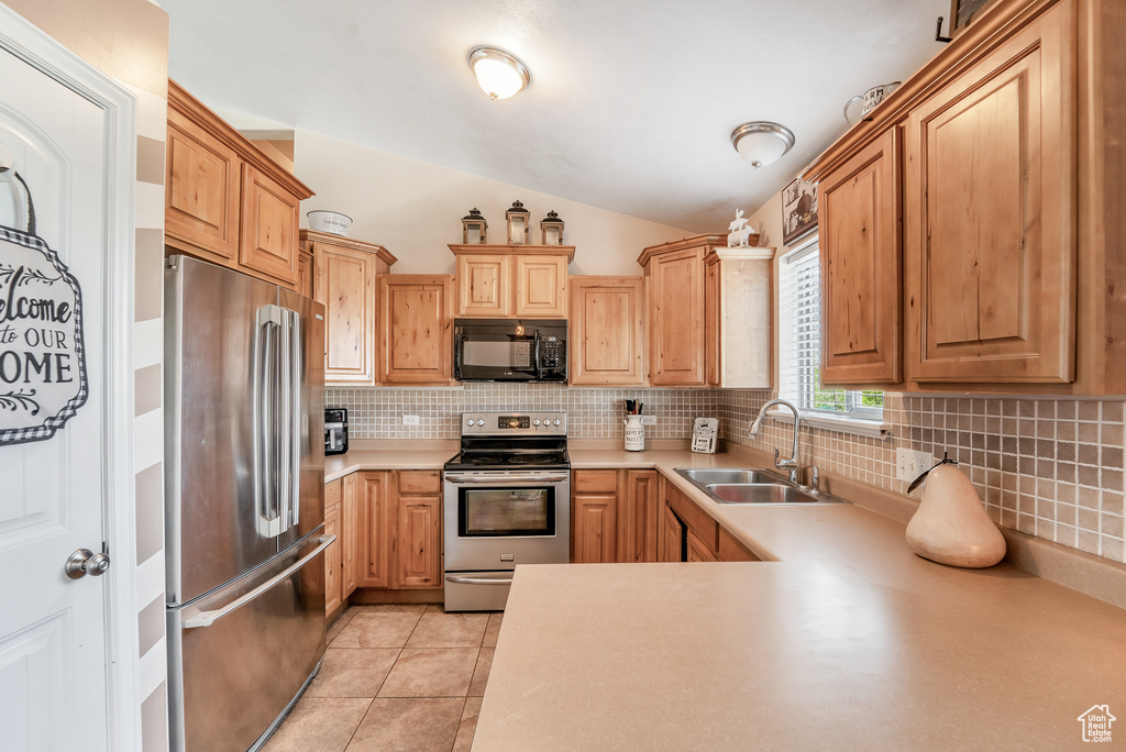 Kitchen featuring backsplash, a sink, appliances with stainless steel finishes, and lofted ceiling