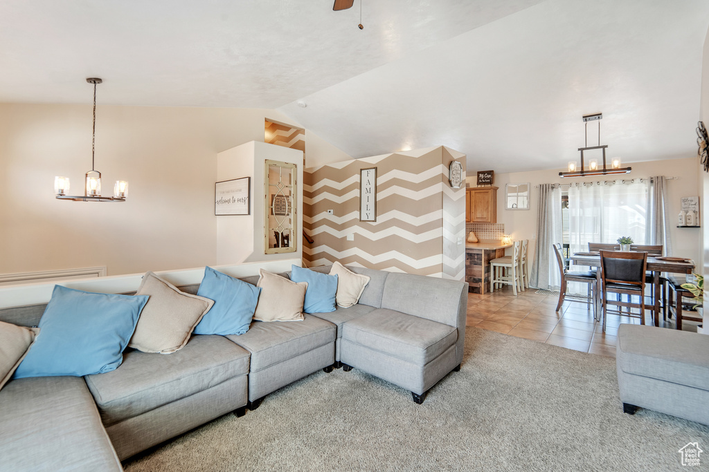 Living room with vaulted ceiling, light tile patterned floors, and ceiling fan with notable chandelier