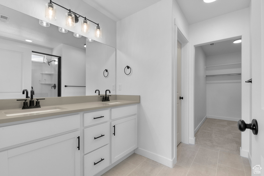 Full bath with double vanity, a walk in closet, baseboards, tile patterned floors, and a shower