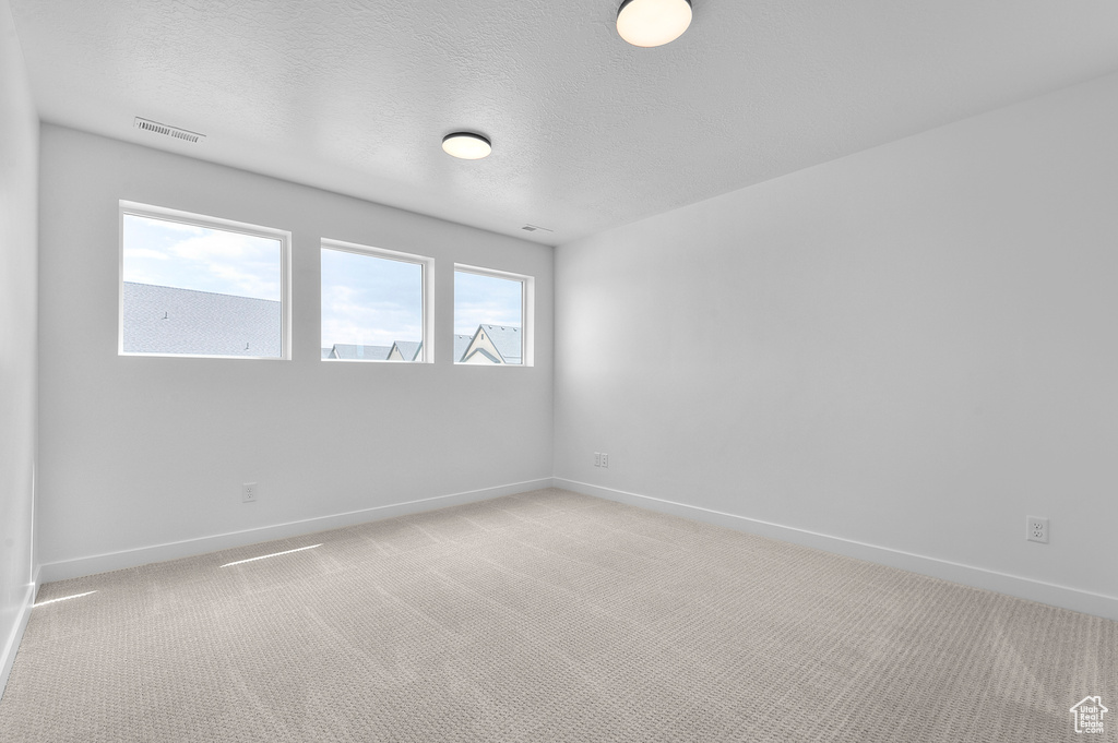 Unfurnished room featuring light carpet, baseboards, and a textured ceiling