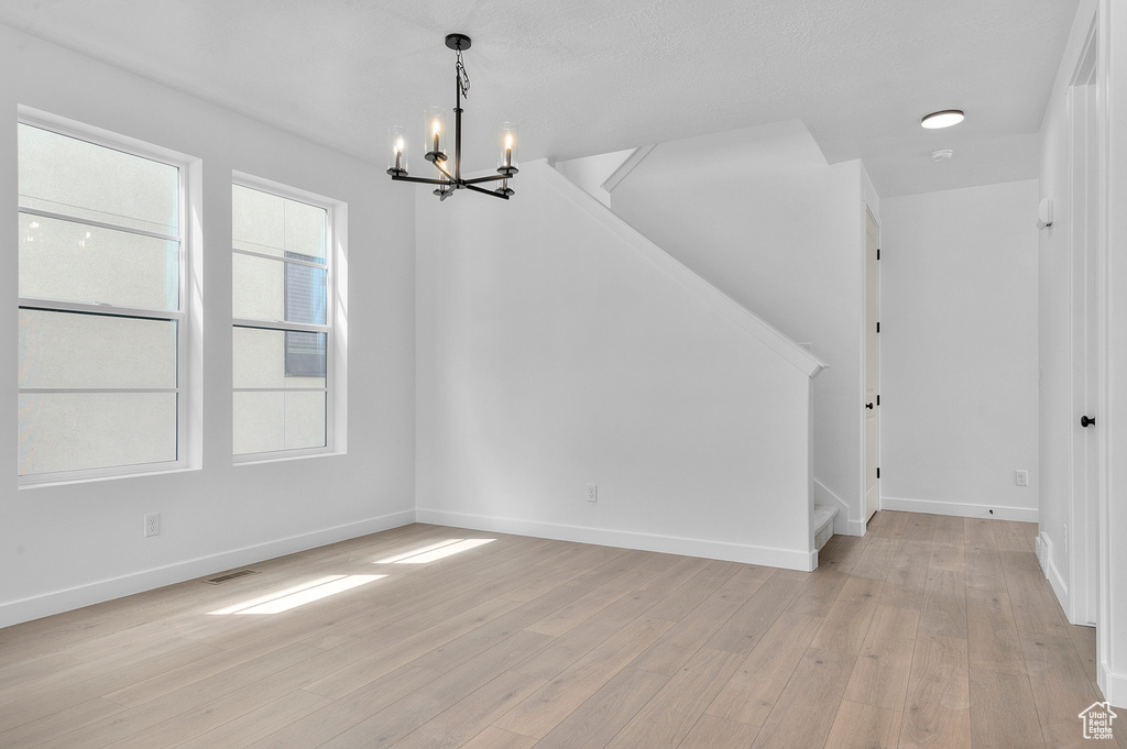 Unfurnished dining area featuring a chandelier, stairway, light wood-style flooring, and baseboards