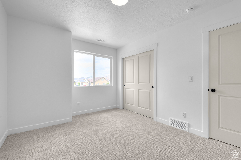 Unfurnished bedroom with light carpet, baseboards, a closet, and a textured ceiling