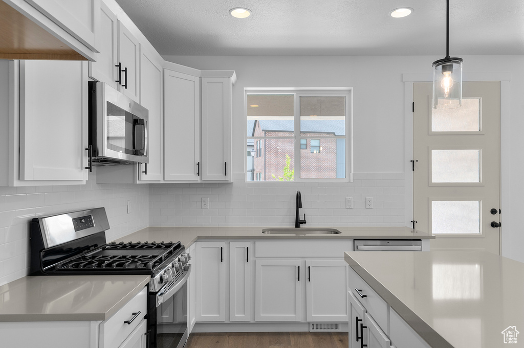 Kitchen with appliances with stainless steel finishes, a sink, light countertops, white cabinets, and backsplash