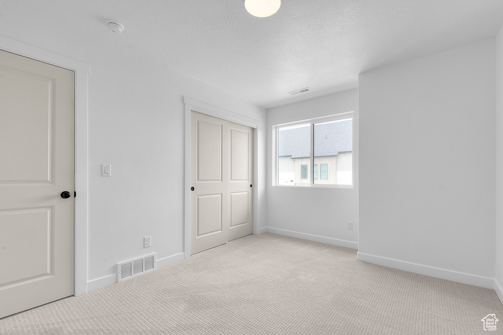 Unfurnished bedroom featuring light carpet, baseboards, a closet, and a textured ceiling