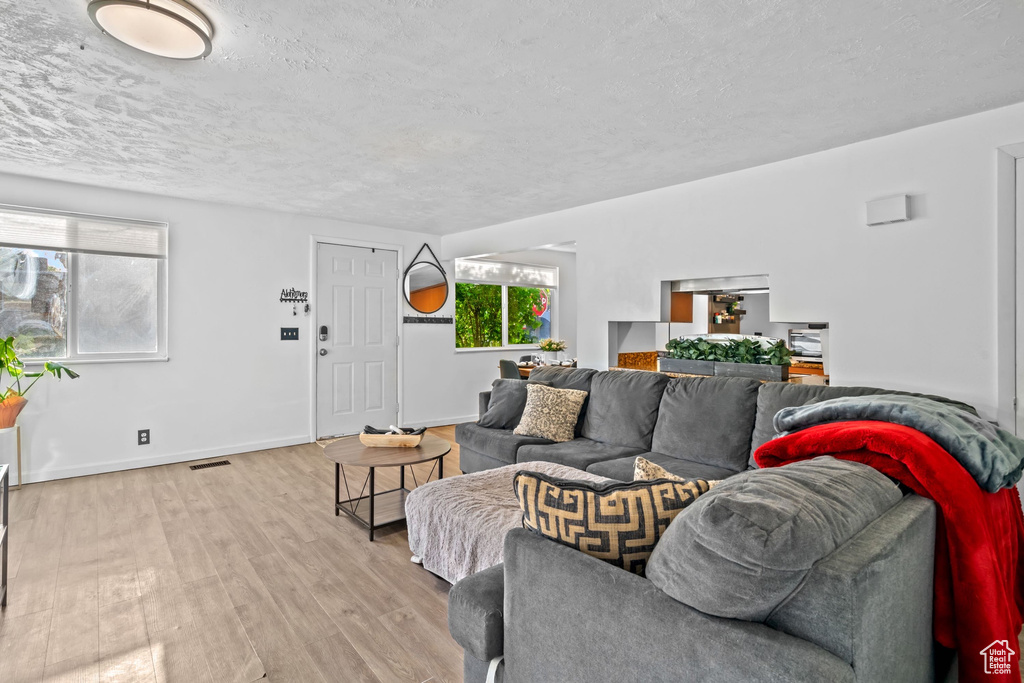 Living room with a textured ceiling, visible vents, baseboards, and light wood-style floors