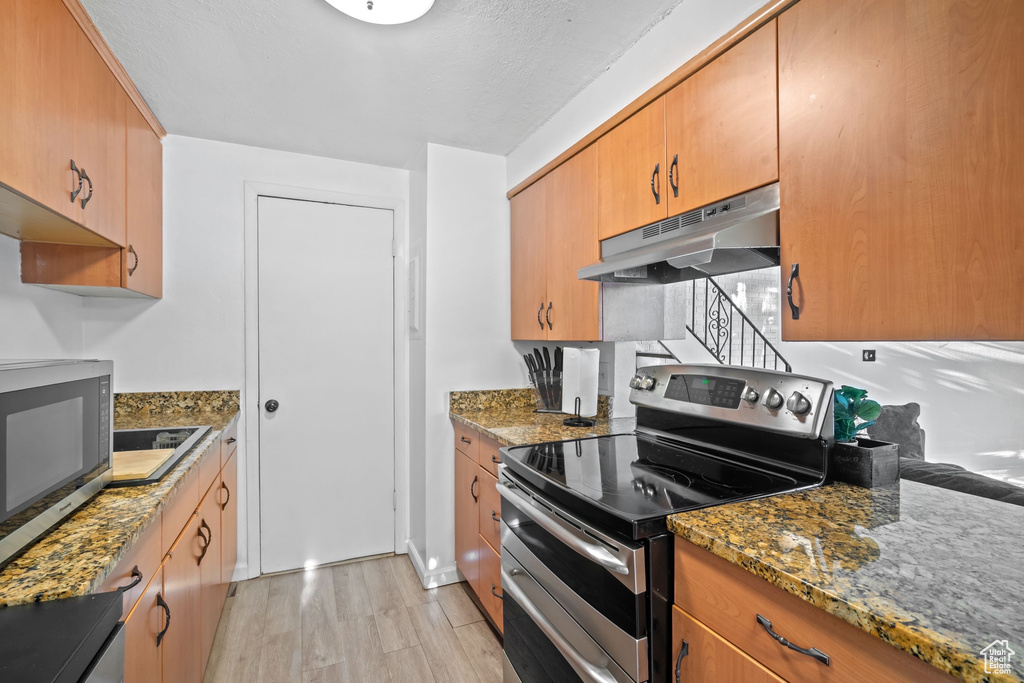 Kitchen with stone countertops, light wood-style flooring, appliances with stainless steel finishes, and under cabinet range hood