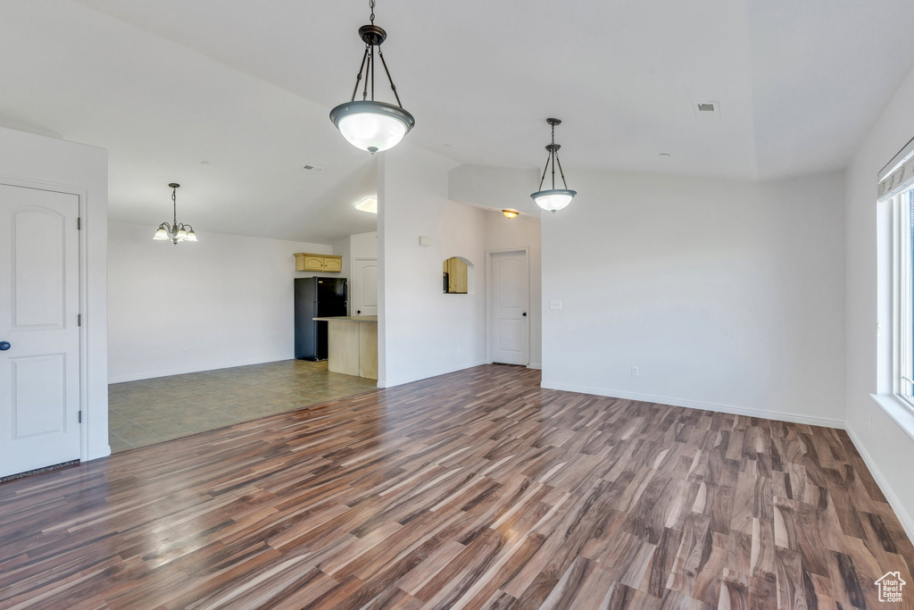 Unfurnished living room featuring an inviting chandelier, vaulted ceiling, wood finished floors, and visible vents