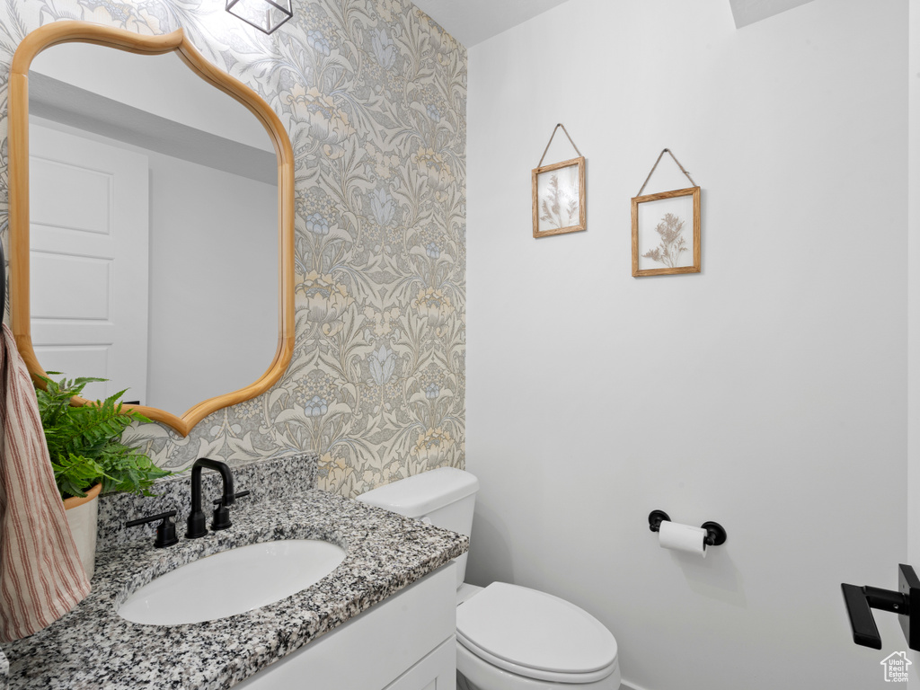 Half bath featuring vanity, baseboards, toilet, and wallpapered walls
