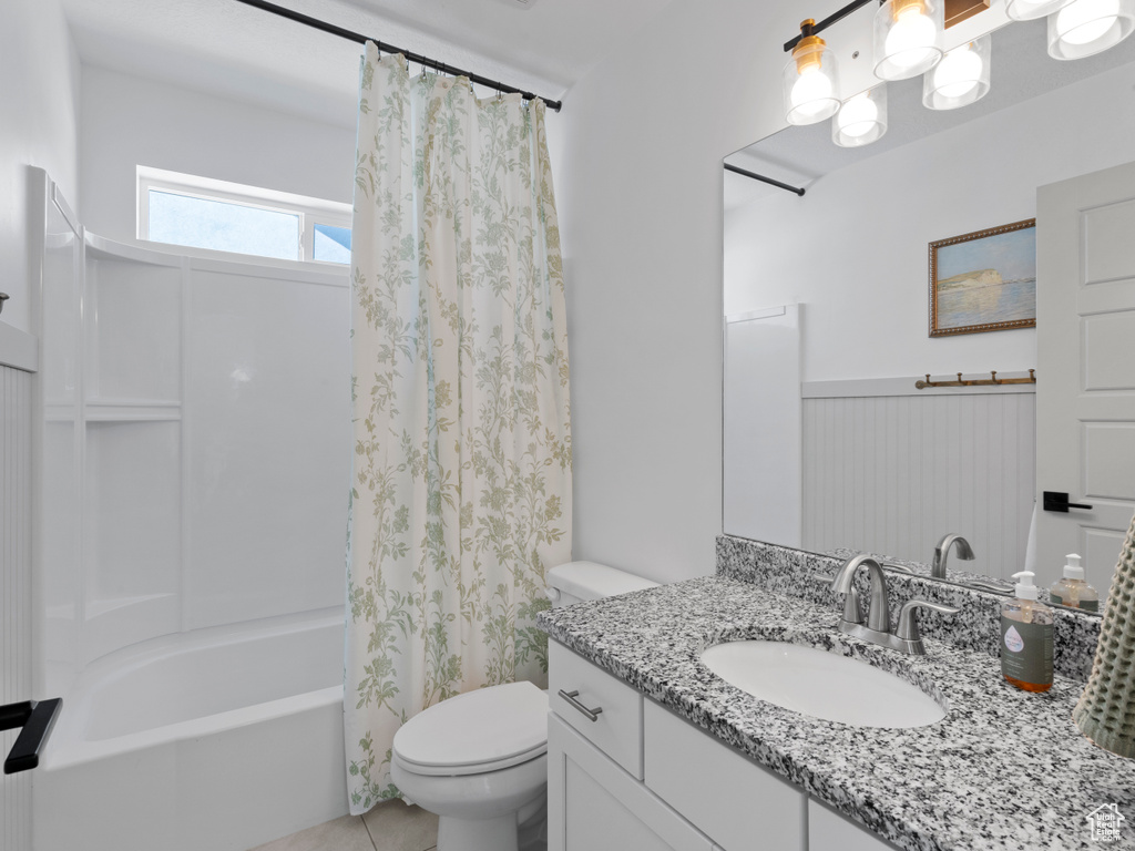 Bathroom with wainscoting, tile patterned flooring, vanity, toilet, and shower / tub combo
