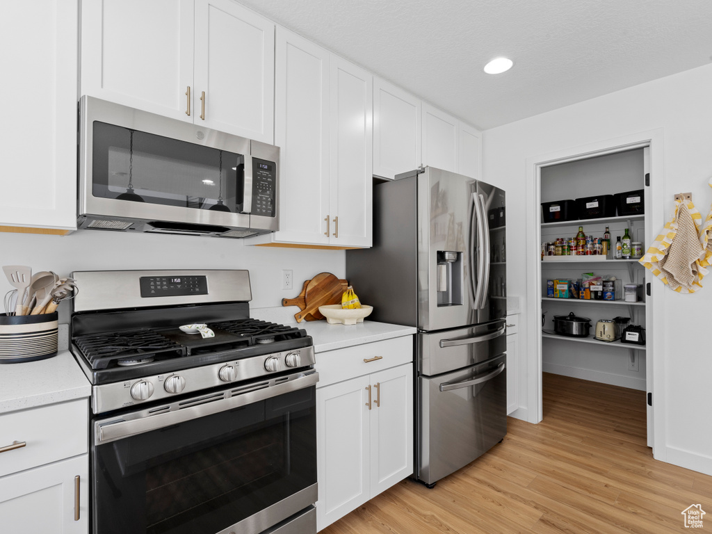 Kitchen with light countertops, white cabinetry, appliances with stainless steel finishes, and light wood-style flooring