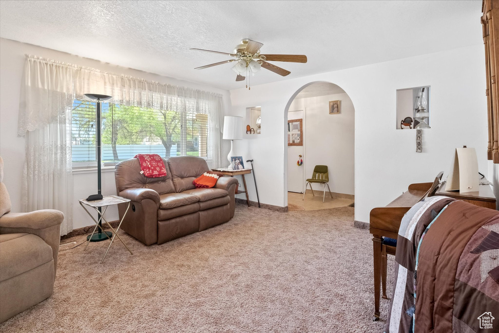 Carpeted living room featuring arched walkways, ceiling fan, baseboards, and a textured ceiling