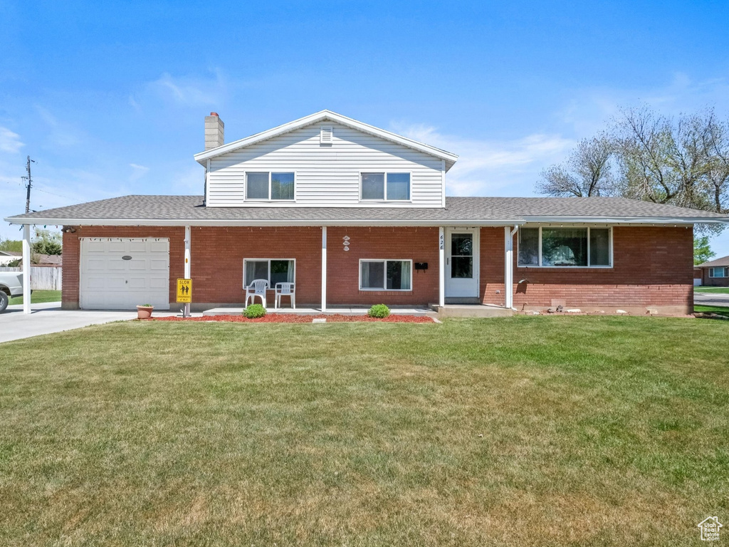 View of front of property featuring a front lawn, brick siding, a garage, a porch, and driveway