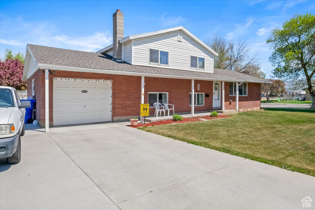 Traditional-style house with a porch, a chimney, a front yard, concrete driveway, and an attached garage