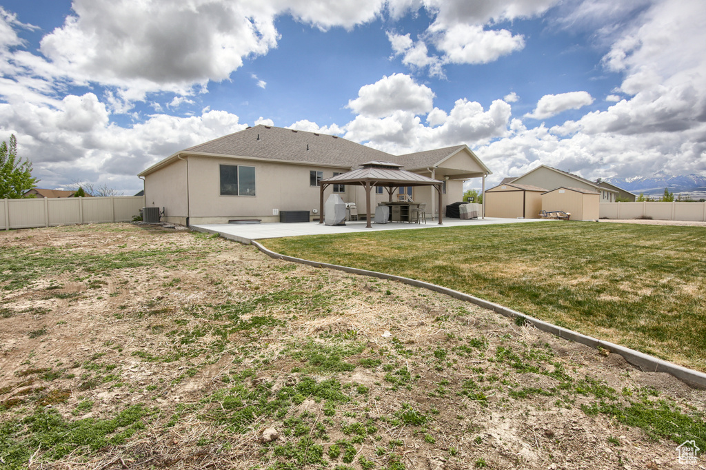 Rear view of house with a fenced backyard, central AC unit, a gazebo, and a patio area