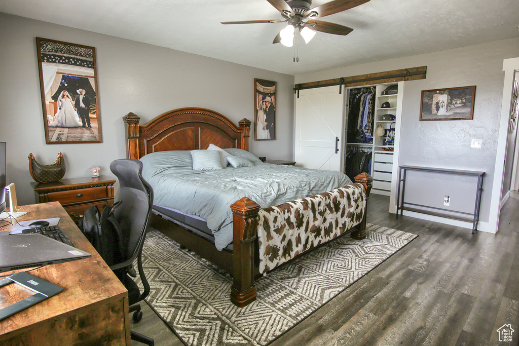 Bedroom featuring ceiling fan, a closet, a barn door, and dark wood-type flooring